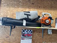 Side view showing full Stihl SH 55 blower with black blower tube and attached collection bag against plywood wall.