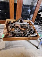 Wooden tray filled with assorted metal bench planes, spokeshaves, wrenches and other hand tools
