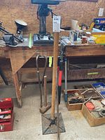 Overview of yard tools including sledgehammer, tamper, crowbars, and loppers standing in front of wooden workbench.