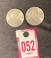 Two 1965 Winston Churchill commemorative crown coins displayed side by side on black fabric with auction tag number 052 visible beneath coins.