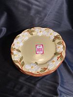 Top-down view of one large plate showing cream background, raised white dogwood flowers with yellow centers and green leaves around rim.