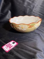 Side view of cream-colored ceramic bowl with scalloped brown rim and raised white dogwood flowers with leaves on the exterior.