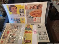 Lot of vintage advertising pages displayed on chair, including Kellogg's Rice Krispies and other cereal ads from mid-1900s.
