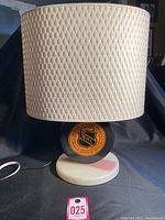Front view of the vintage NHL lamp showing the textured cream-white lampshade and round black base resembling a hockey puck with the NHL logo.