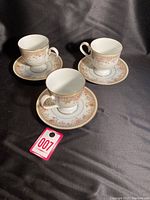 Set of three porcelain cups on matching saucers with floral decoration and gold edging.