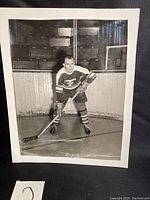 Full view of vintage black and white hockey photo showing player on ice with rink boards and empty bleachers in background.