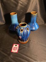 Front view of three blue glazed Denby vases, two identical tall vases and one smaller vase with multiple holes, displayed against black background.