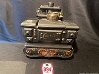 Front view of the vintage black stove cookie jar with lid and kettle detail on top, showcasing detailed mold and orange decorative painting on base.