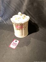 Front view of ceramic tea canister with floral design and lid on black background.