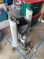 Two white Sharper Image SI637 tower air purifiers and one gray smaller tower air purifier with rotary dial, along with a black Pollenex air cleaner box, and fan.