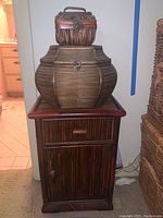 Front view of bamboo cabinet with drawer and door, large bulbous wicker basket with latch, and small wicker basket box with handle on top.