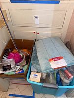 Bin full of folded bath mats, towels, and assorted bath accessories including a blood pressure monitor and plastic bottles.