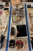 Full overview of assorted costume jewelry laid out on a white surface showing boxes, bracelets, earrings, necklaces, and pins.
