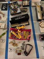 Overall display of assorted costume jewelry on table including necklaces, bracelets, earrings, and pins. Variety of styles and colors.
