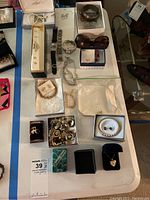 Overview of many items including boxed pearl necklace, watches, bracelets, earrings, and loose charms on table