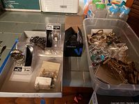 Lot layout showing watches, costume jewelry, necklaces and earrings spread on trays and in a plastic bin.