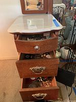 Photo of open wooden drawer unit showing three drawers filled with costume jewelry items.