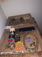 Two cardboard trays containing the costume jewelry lot items arranged for photography, showing bracelets, necklaces, pins, and earrings in varied styles and colors.