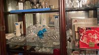 Glass and crystal bowls, vases, and blue glass salt and pepper shakers inside display cabinet