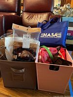 Photo of two fabric bins containing assorted bags, packaged hair extensions including one box labeled Closure, and a blue tote bag with white text PHASA.