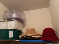 Photo showing various hat storage boxes stacked on a shelf with the red felt cloche hat and the woven straw hat placed on top.