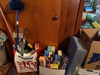 Photo shows a variety of cleaning supplies including a blue handled duster and multiple boxes and bags filled with cleaning and kitchen storage products.