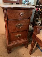 Front view of oak pedestal vanity showing three drawers, marble top and ornate hardware
