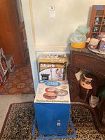 Two boxed cleaning products in a room: Shark Lift Away Pro Steam Pocket Mop and Hurricane Spin Mop.