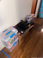 Showing overall lot with stacked plastic storage containers filled with office supplies and some cardboard boxes.