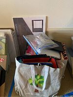 Photo showing a bag containing assorted folders, binders, and notebooks with a large Ghostline tri-fold display board behind.