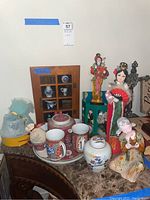 Photo showing oriental tea set with cups and matching ginger jar, three figurines, and wooden display case with miniature items on marble surface