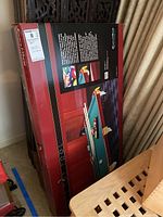 Photo of a boxed table top pool table featuring an image of the table with green felt, wooden frame, pockets with tassels, pool balls, and pool cues displayed on the box surface.