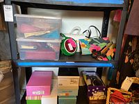 Shelf showing plastic containers with purses inside and additional items including a floral print handbag and several pairs of shoes.