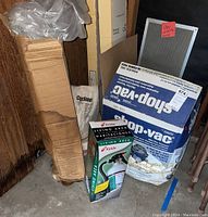 Photo shows boxed Shop Vac vacuum, Kidde fire extinguisher box, roll of plastic sheeting, and car accessories in brown cardboard boxes.