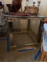 Front view of glass top side table with metal legs, carpeted background and various decorative items placed on top.