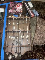 Wooden holder with multiple silverplated spoons displayed, showing various designs and sizes.