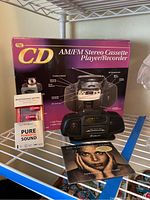 Photo showing the AM/FM stereo cassette player/recorder model ATC-60 in its original box along with initial earphones with microphone and CD album in front