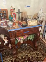 Front view of the wood table with marble top showing carved details, drawer and decoration on a patterned rug.