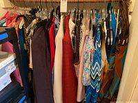 Wide view of multiple women's clothing items hung on hangers including dresses, slacks, and blouses in various colors and patterns.