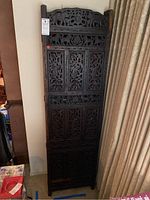 Front view of one dark wood carved panel of the folding room divider, shows detailed floral and geometric carving with an arched top.