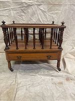 Front view of 19th century rosewood Canterbury showing rectangular form, turned spindles, drawer, and caster wheels.
