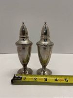 Front view of two sterling silver salt and pepper shakers with measuring tape showing length around 5.5 inches