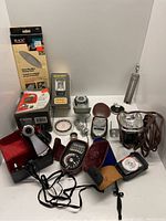 Full view of all camera accessories including light meters, flash units, cleaning pouch, cases, and other accessories arranged on a flat surface.