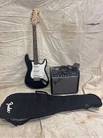 Front view of black Fender Squier Stratocaster electric guitar, Fender amp, and Fender gig bag