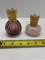 Front view of two diffuser lamps side by side with measuring tape showing size, purple ribbed glass on left, iridescent pink round glass on right