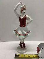 Front view of the Hollohaza porcelain figurine showing the dancer's pose and details of the dress and headpiece with measuring tape showing approximate height.