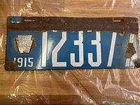 Front of the 1915 Pennsylvania license plate showing blue background, white embossed numbers 12337, keystone emblem, rust on top and edges.