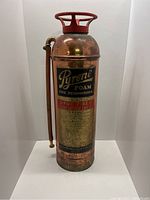 Front view of copper Pyrene foam fire extinguisher with attached hose and valve handle.