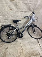 Photo shows full side view of white Schwinn Hydra bicycle with front suspension, rear rack, and black seat against a beige background.