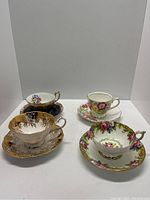 Four vintage porcelain tea cups and saucers with varied floral and gold designs, displayed against a white background.